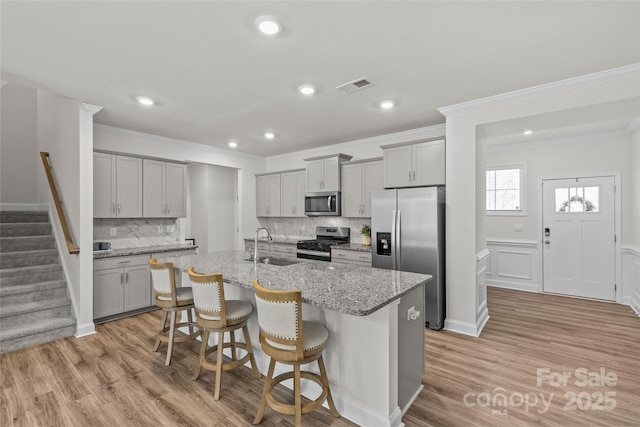 kitchen with a breakfast bar, a kitchen island with sink, sink, light stone countertops, and stainless steel appliances