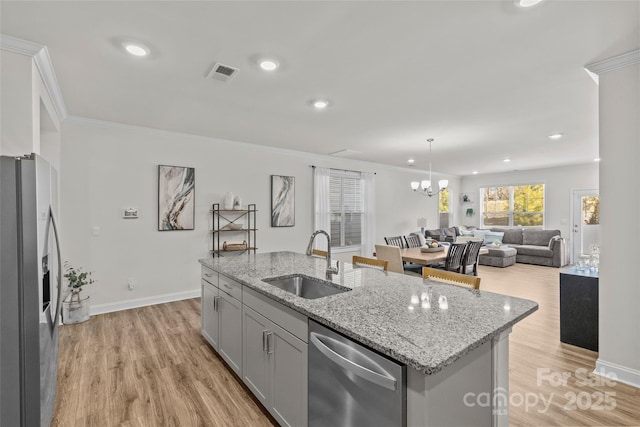 kitchen featuring a kitchen island with sink, sink, light stone counters, and appliances with stainless steel finishes