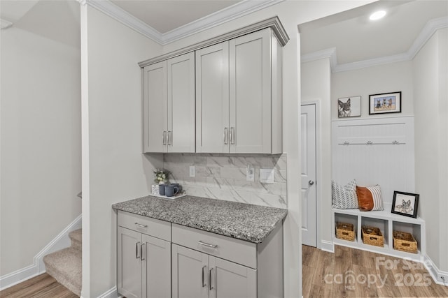 kitchen featuring light stone countertops, tasteful backsplash, gray cabinetry, crown molding, and dark wood-type flooring