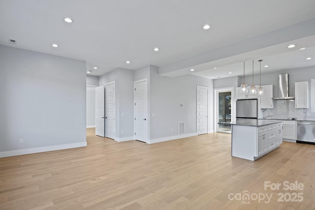 kitchen with appliances with stainless steel finishes, wall chimney exhaust hood, a kitchen island, white cabinetry, and hanging light fixtures