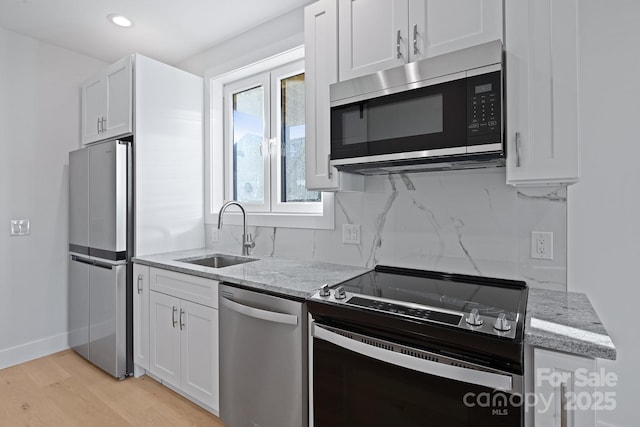 kitchen with light stone countertops, appliances with stainless steel finishes, light wood-type flooring, sink, and white cabinets