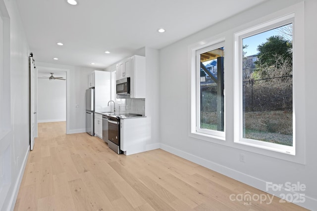 kitchen with white cabinetry, a wealth of natural light, a barn door, backsplash, and appliances with stainless steel finishes