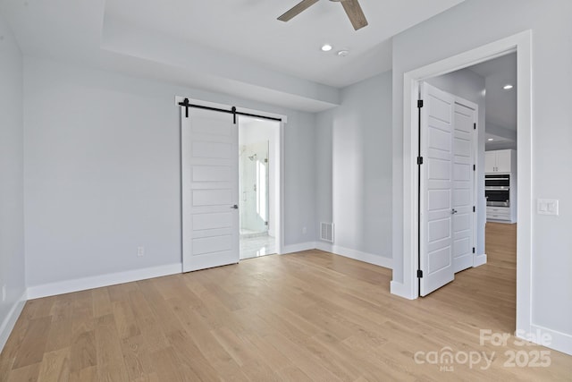 empty room with ceiling fan, a barn door, and light hardwood / wood-style flooring