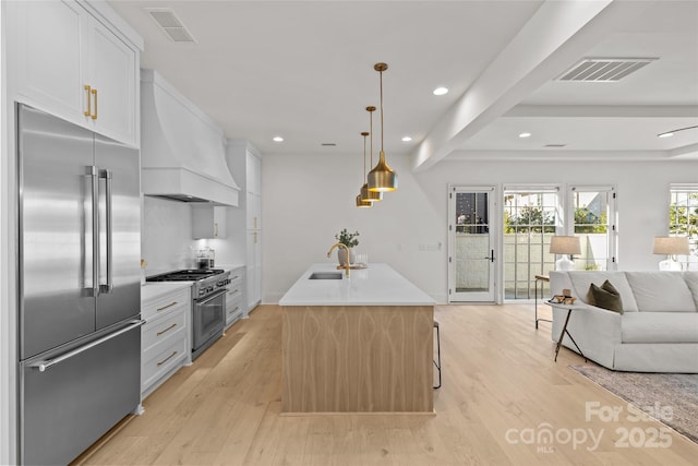 kitchen with a kitchen island with sink, custom exhaust hood, white cabinets, and high end appliances