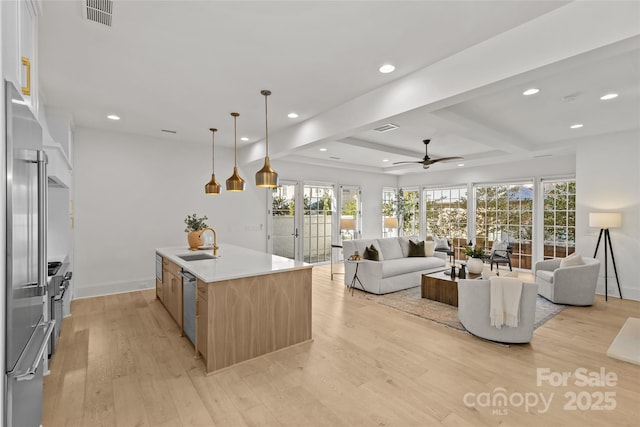 kitchen with sink, stainless steel appliances, decorative light fixtures, beamed ceiling, and a kitchen island with sink