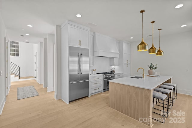 kitchen featuring sink, white cabinetry, custom range hood, a center island with sink, and premium appliances