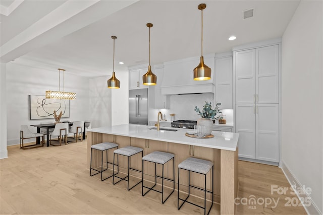 kitchen with sink, built in fridge, a large island, white cabinets, and pendant lighting