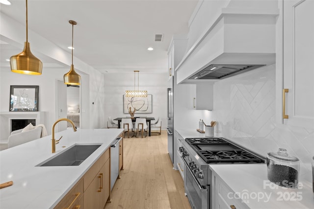 kitchen with stainless steel appliances, custom range hood, white cabinets, decorative light fixtures, and sink