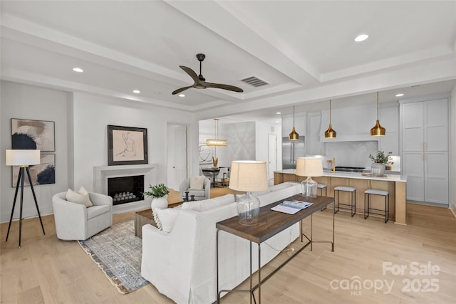 living room featuring ceiling fan, light hardwood / wood-style floors, and beamed ceiling