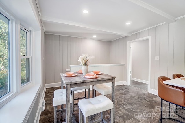 dining space with beamed ceiling, ornamental molding, plenty of natural light, and wood walls