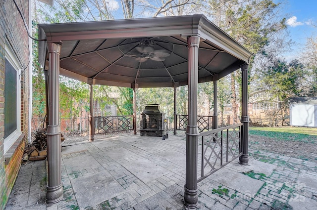 view of patio featuring a gazebo, ceiling fan, an outdoor stone fireplace, and a storage unit