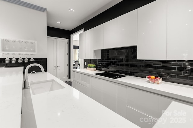 kitchen featuring sink, white cabinetry, black electric stovetop, light stone countertops, and backsplash