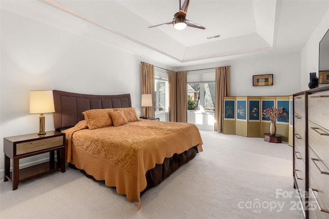 carpeted bedroom featuring ceiling fan and a raised ceiling