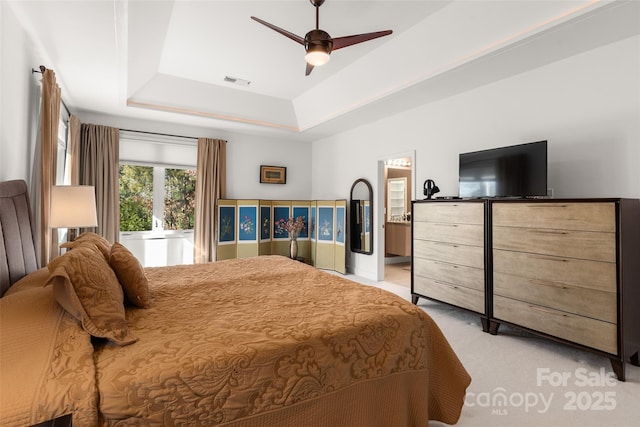 carpeted bedroom with ensuite bathroom, ceiling fan, and a tray ceiling