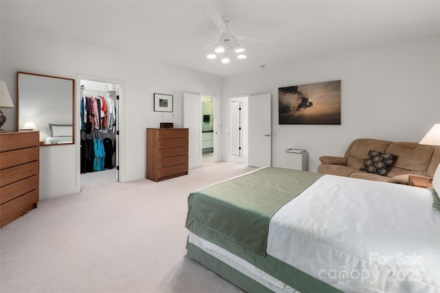 bedroom with ceiling fan, ensuite bathroom, a spacious closet, light colored carpet, and a closet