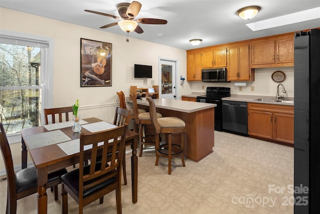 kitchen featuring ceiling fan, black appliances, a kitchen bar, kitchen peninsula, and sink