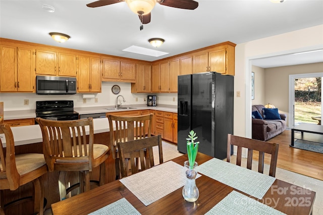 kitchen featuring a skylight, light hardwood / wood-style floors, ceiling fan, black appliances, and sink