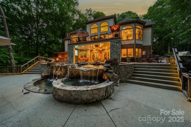 back house at dusk featuring a balcony and a patio area