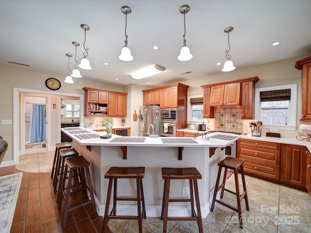 kitchen featuring a breakfast bar, appliances with stainless steel finishes, a center island with sink, and tasteful backsplash