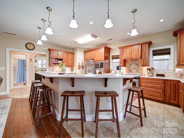 kitchen with backsplash, a kitchen breakfast bar, an island with sink, appliances with stainless steel finishes, and decorative light fixtures