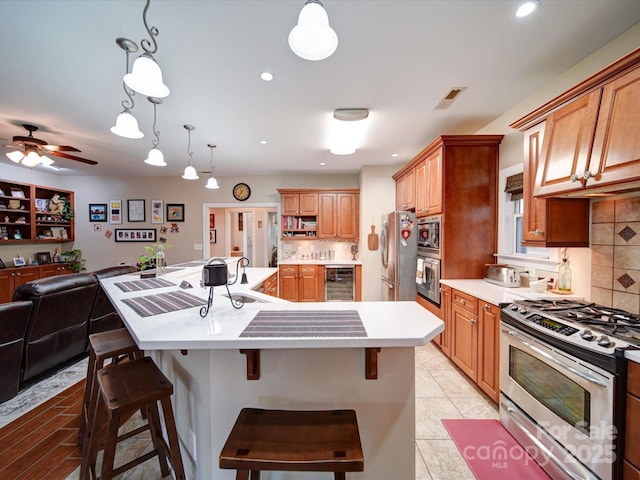 kitchen featuring appliances with stainless steel finishes, tasteful backsplash, beverage cooler, a center island with sink, and a breakfast bar area