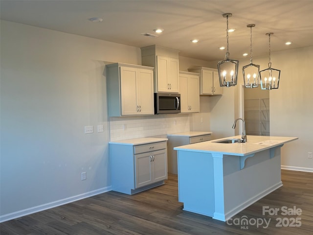 kitchen featuring tasteful backsplash, a kitchen island with sink, sink, dark hardwood / wood-style floors, and hanging light fixtures