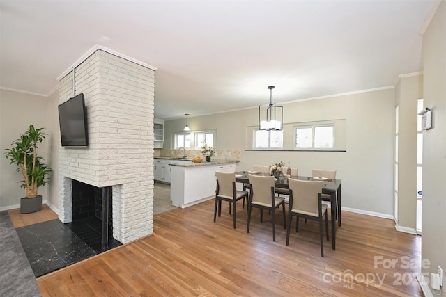 dining space featuring light wood-type flooring, a brick fireplace, sink, ornamental molding, and a chandelier