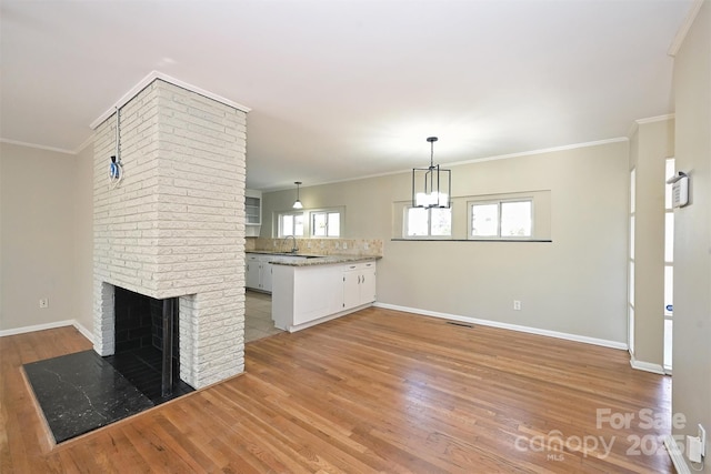 unfurnished living room featuring a brick fireplace, a notable chandelier, light hardwood / wood-style floors, sink, and crown molding