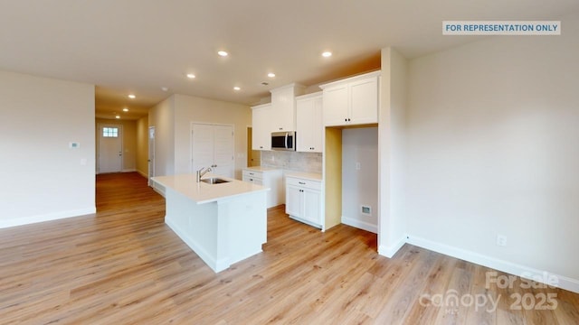 kitchen with sink, an island with sink, light hardwood / wood-style floors, decorative backsplash, and white cabinets