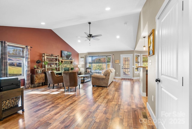 living room featuring wood-type flooring, high vaulted ceiling, a stone fireplace, and ceiling fan