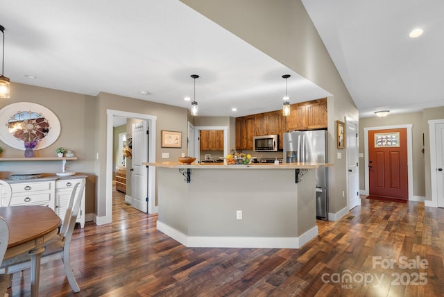 kitchen featuring a kitchen bar, dark hardwood / wood-style flooring, hanging light fixtures, and appliances with stainless steel finishes