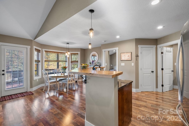 kitchen featuring pendant lighting, vaulted ceiling, light hardwood / wood-style flooring, stainless steel fridge, and a textured ceiling