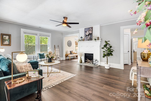 living room featuring ceiling fan, ornamental molding, dark wood-type flooring, and a brick fireplace