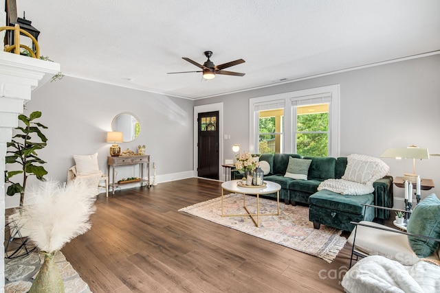 living room featuring ceiling fan, a stone fireplace, dark hardwood / wood-style flooring, and ornamental molding