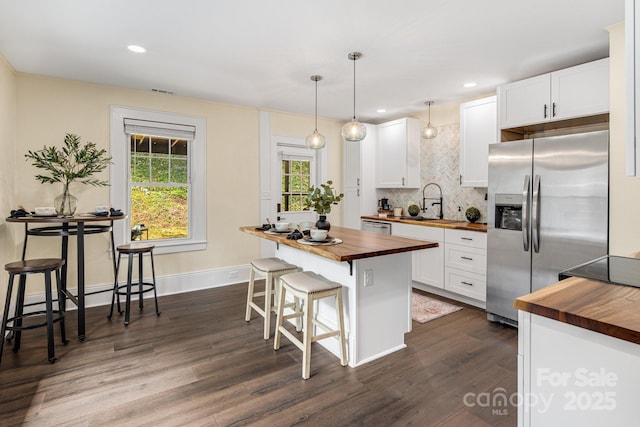 kitchen featuring a breakfast bar, appliances with stainless steel finishes, white cabinets, and butcher block counters