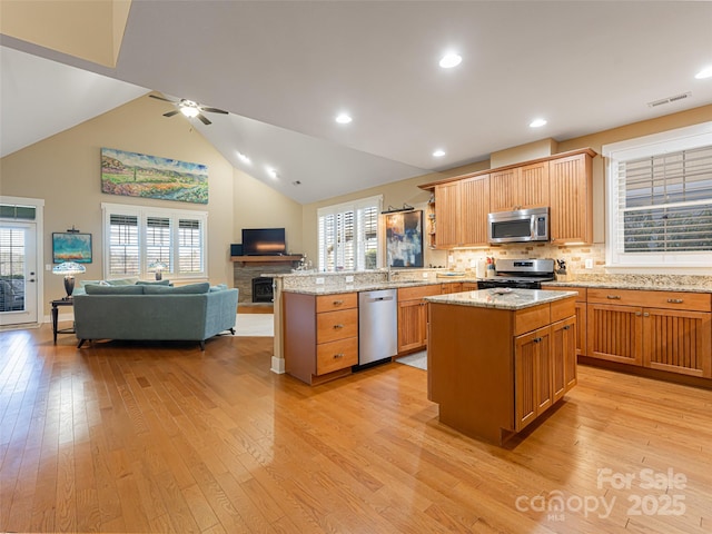 kitchen with kitchen peninsula, appliances with stainless steel finishes, light wood-type flooring, and a center island