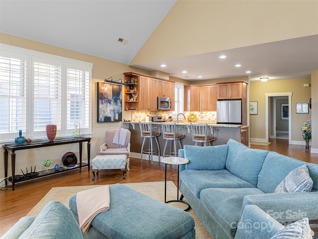 living room with light hardwood / wood-style floors, sink, and high vaulted ceiling