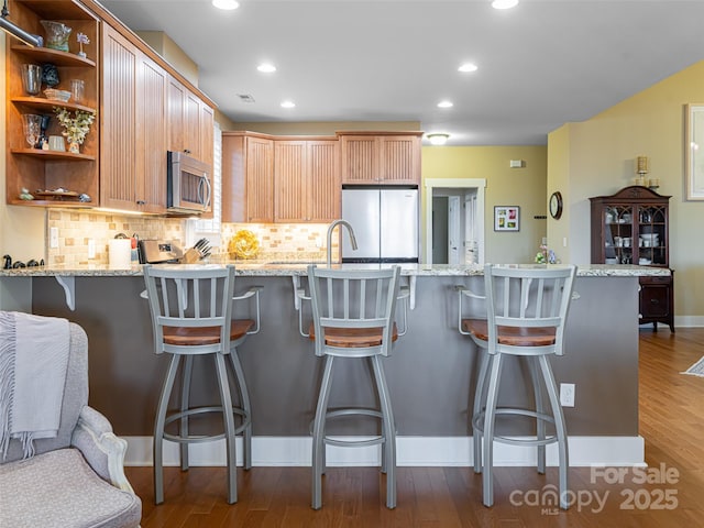 kitchen with appliances with stainless steel finishes, dark hardwood / wood-style flooring, tasteful backsplash, light stone counters, and a breakfast bar