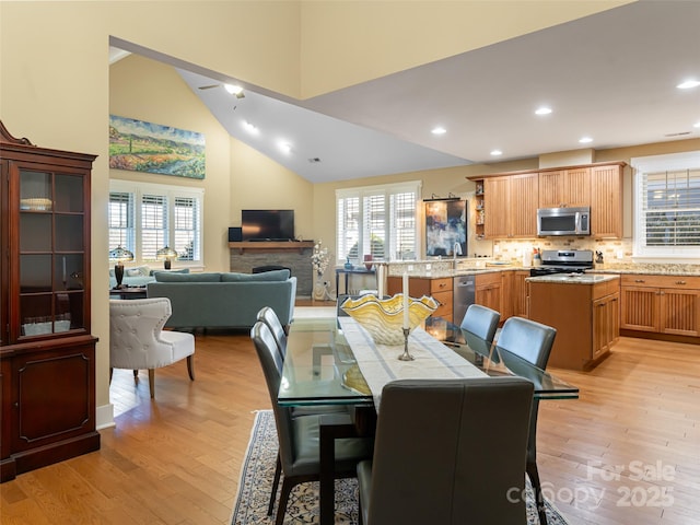 dining space with a fireplace, light wood-type flooring, high vaulted ceiling, and sink