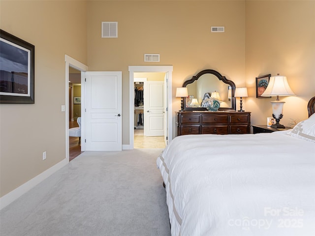 carpeted bedroom with ensuite bathroom, a towering ceiling, and a spacious closet