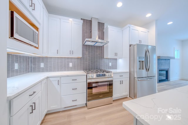 kitchen featuring backsplash, wall chimney exhaust hood, light hardwood / wood-style floors, white cabinetry, and stainless steel appliances