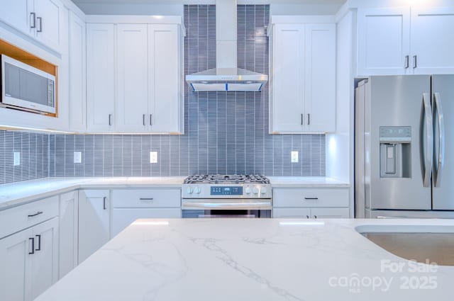 kitchen featuring stainless steel appliances, light stone counters, ventilation hood, backsplash, and white cabinets