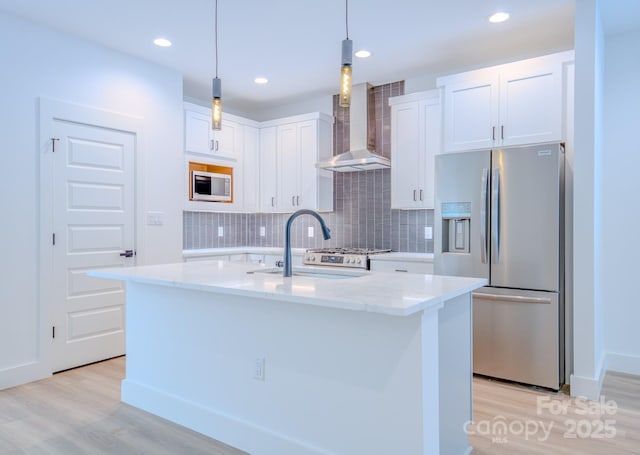 kitchen featuring stainless steel refrigerator with ice dispenser, built in microwave, wall chimney range hood, white cabinetry, and an island with sink