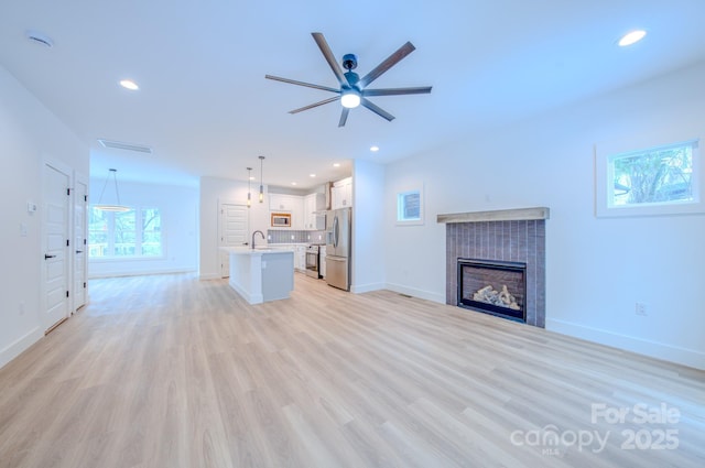 unfurnished living room with ceiling fan, light wood-type flooring, and sink