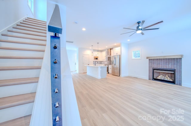 unfurnished living room with ceiling fan, sink, and light hardwood / wood-style flooring