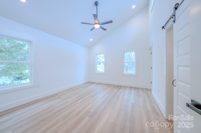 unfurnished room featuring a barn door, ceiling fan, high vaulted ceiling, and light hardwood / wood-style floors