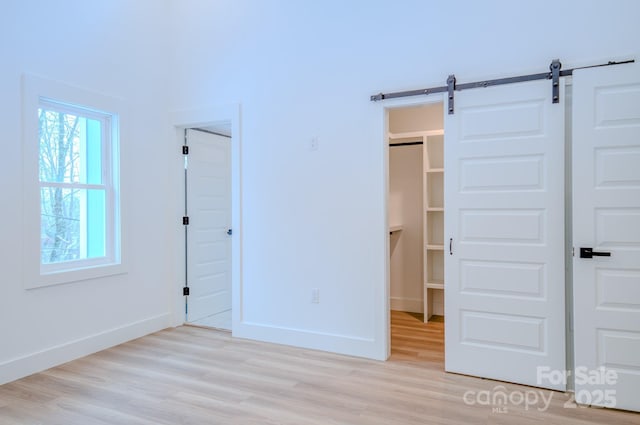 unfurnished bedroom featuring a barn door, a closet, and light wood-type flooring