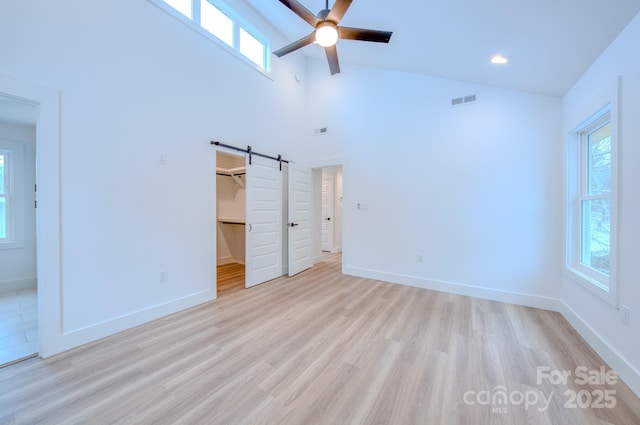 unfurnished bedroom featuring ceiling fan, a barn door, light hardwood / wood-style flooring, a walk in closet, and a closet