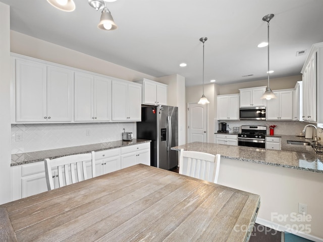 kitchen with stainless steel appliances, sink, decorative light fixtures, dark stone countertops, and white cabinetry