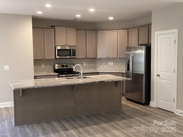 kitchen featuring a center island with sink, dark hardwood / wood-style flooring, light stone countertops, and stainless steel appliances